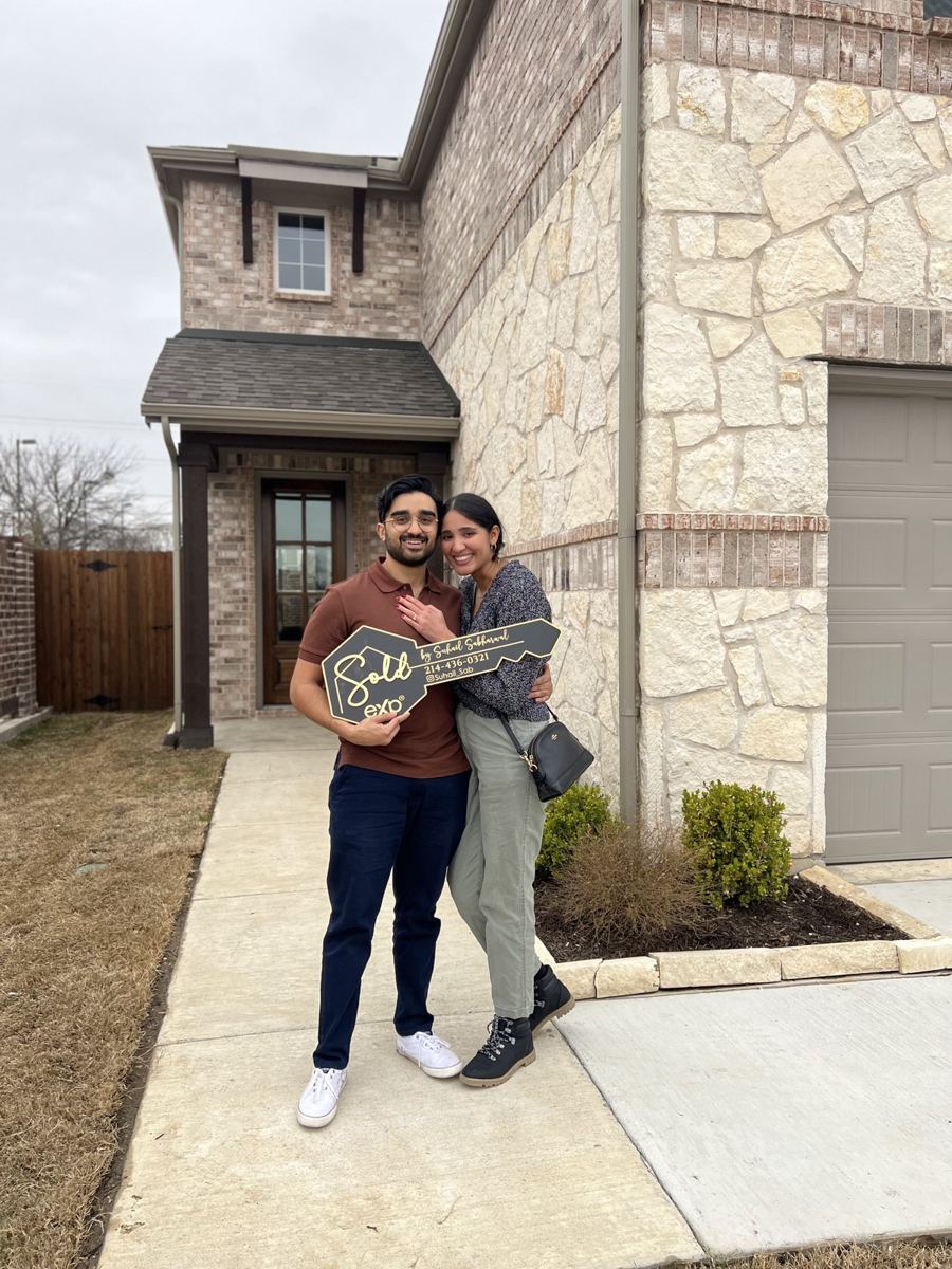 Couple holding a sold sign outside their new stone and brick home
