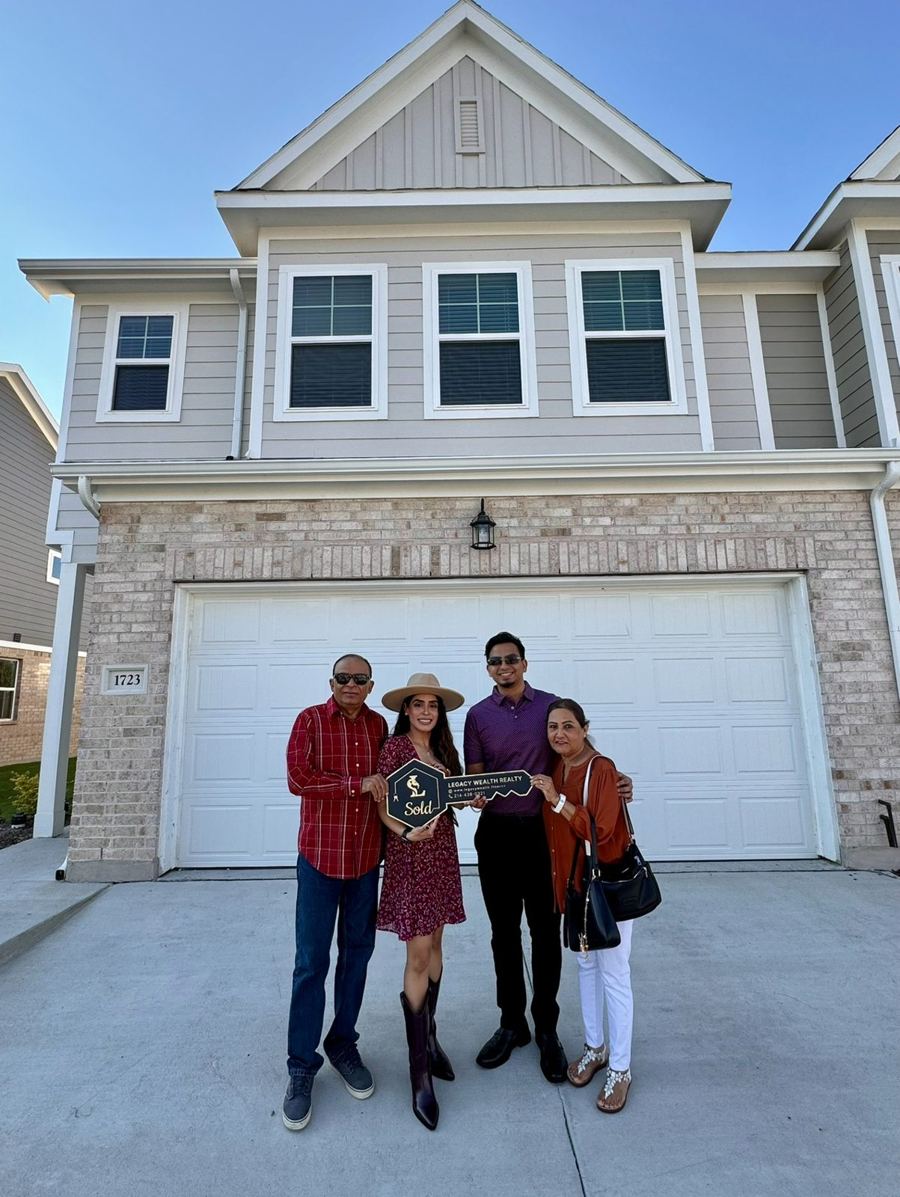 Family celebrating with a Legacy Wealth Realty sold sign in front of their new townhome