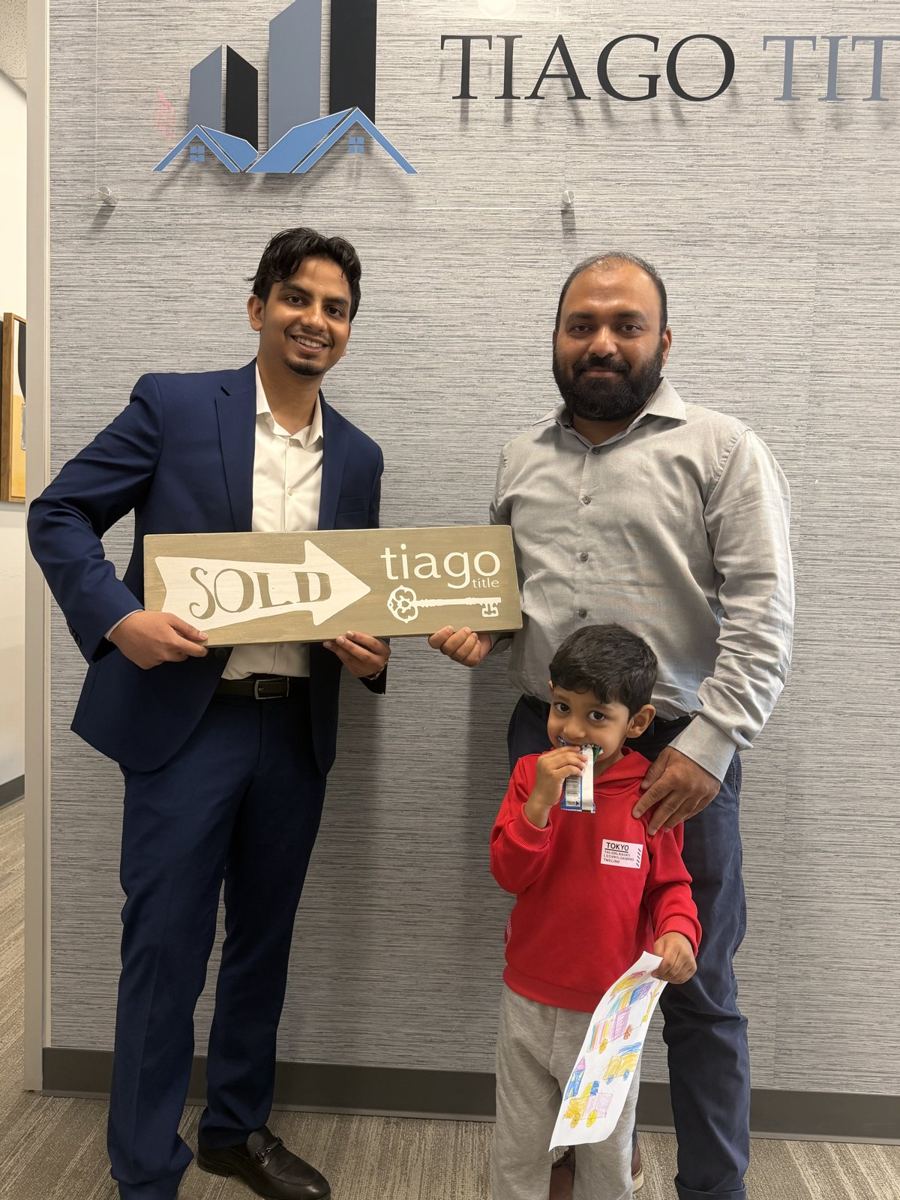 Suhail with a buyer and his son holding a sold sign at the title company